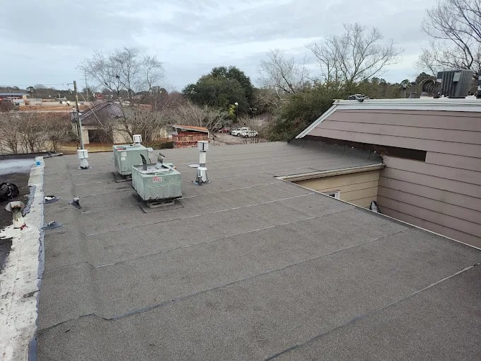 Flat rooftop with HVAC units, surrounded by trees and buildings on cloudy day