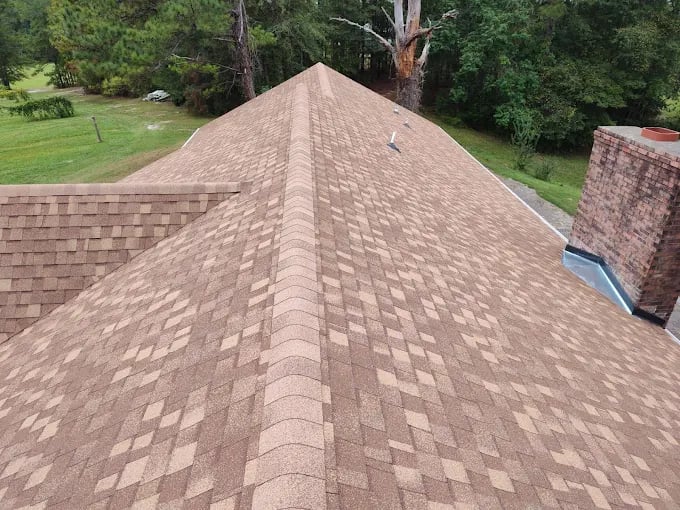 Aerial view of a brown asphalt shingle roof with brick chimney near trees