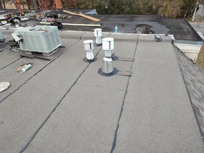 Commercial flat roof with HVAC unit, ventilation pipes, and seam lines