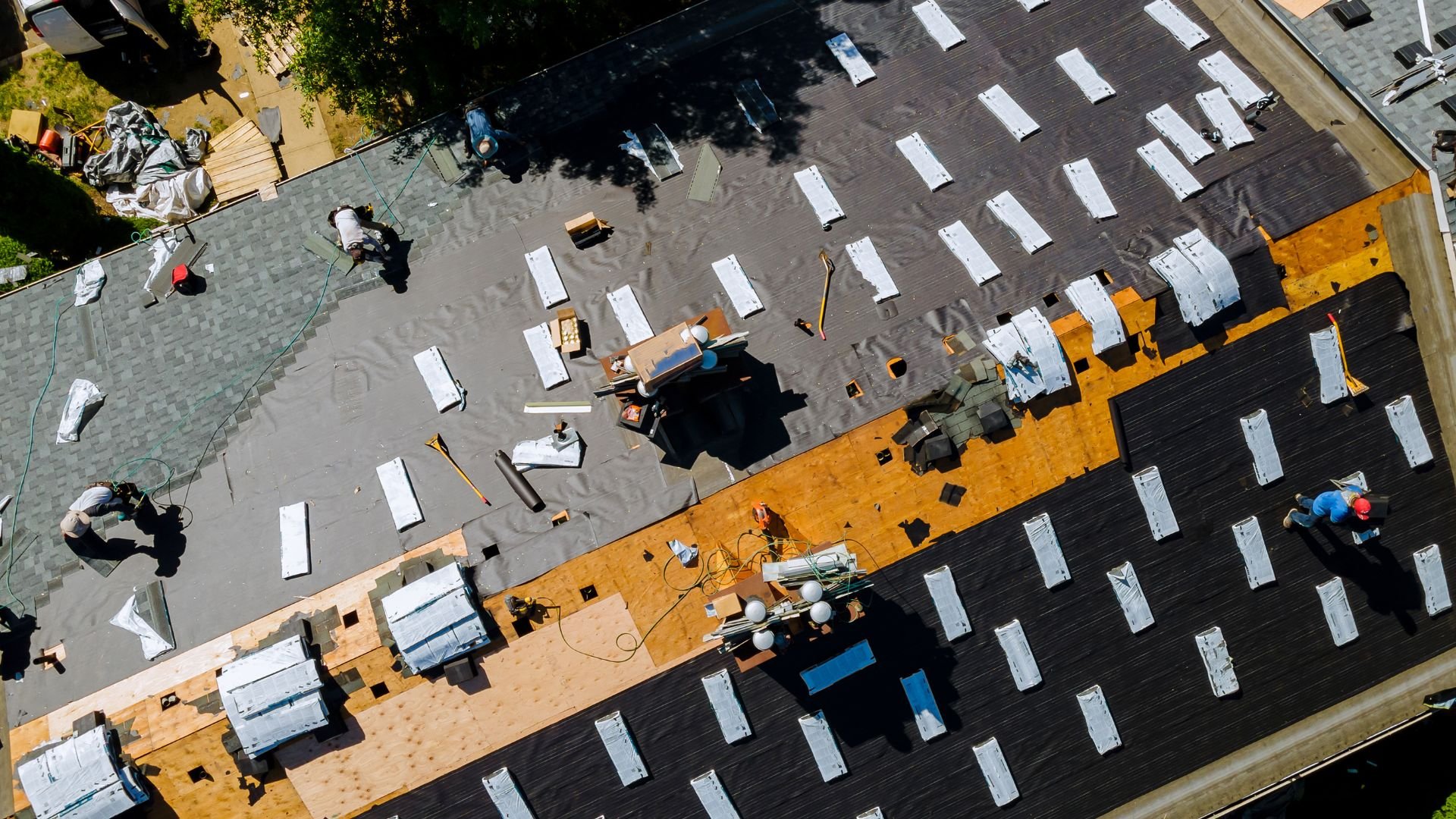 Aerial view of roofers installing shingles on a large residential roof