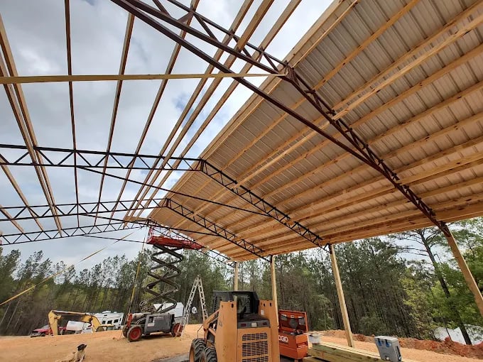 Metal roof truss construction site with heavy machinery and equipment