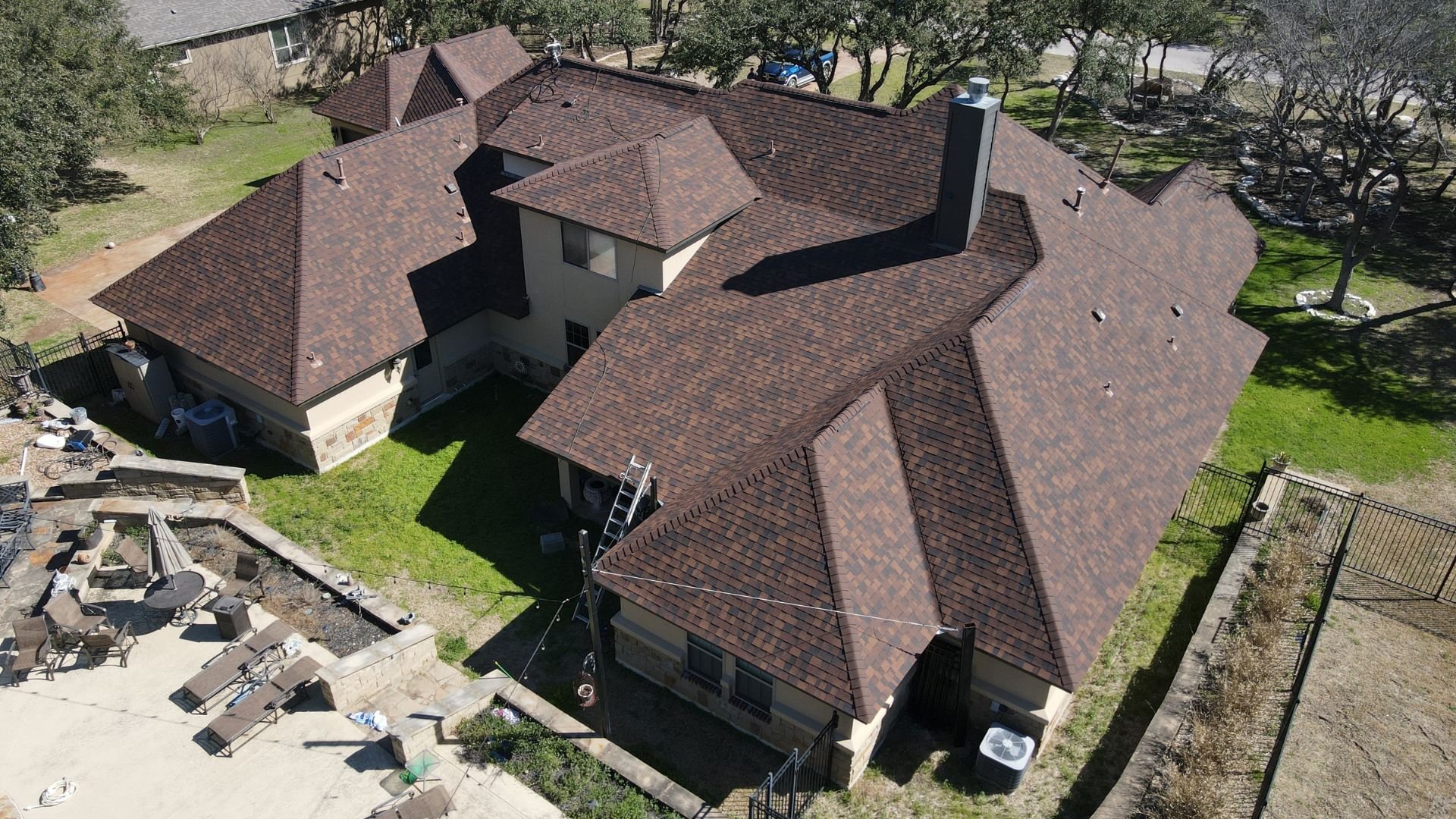 Aerial view of large suburban home with complex brown roof and construction area