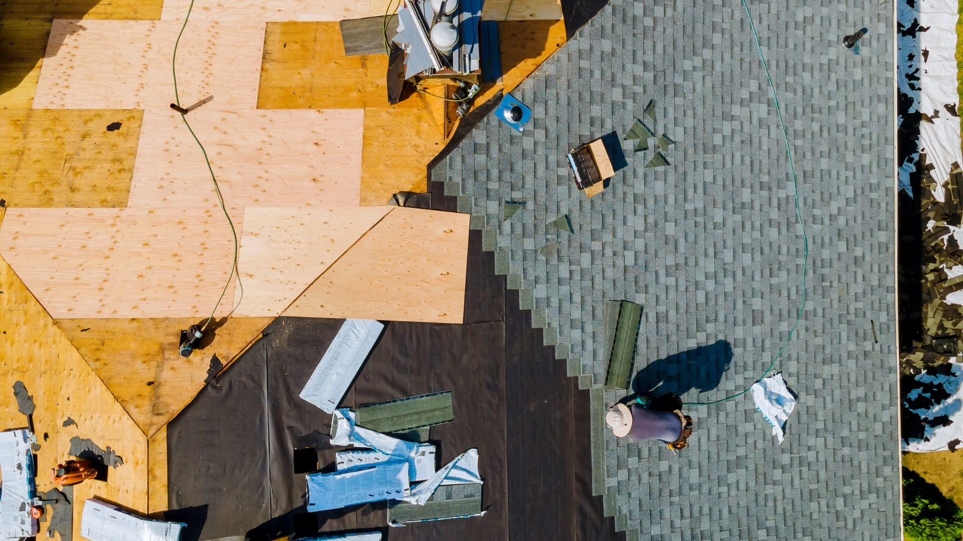 Aerial view of construction site with plywood, roofing materials, and workers
