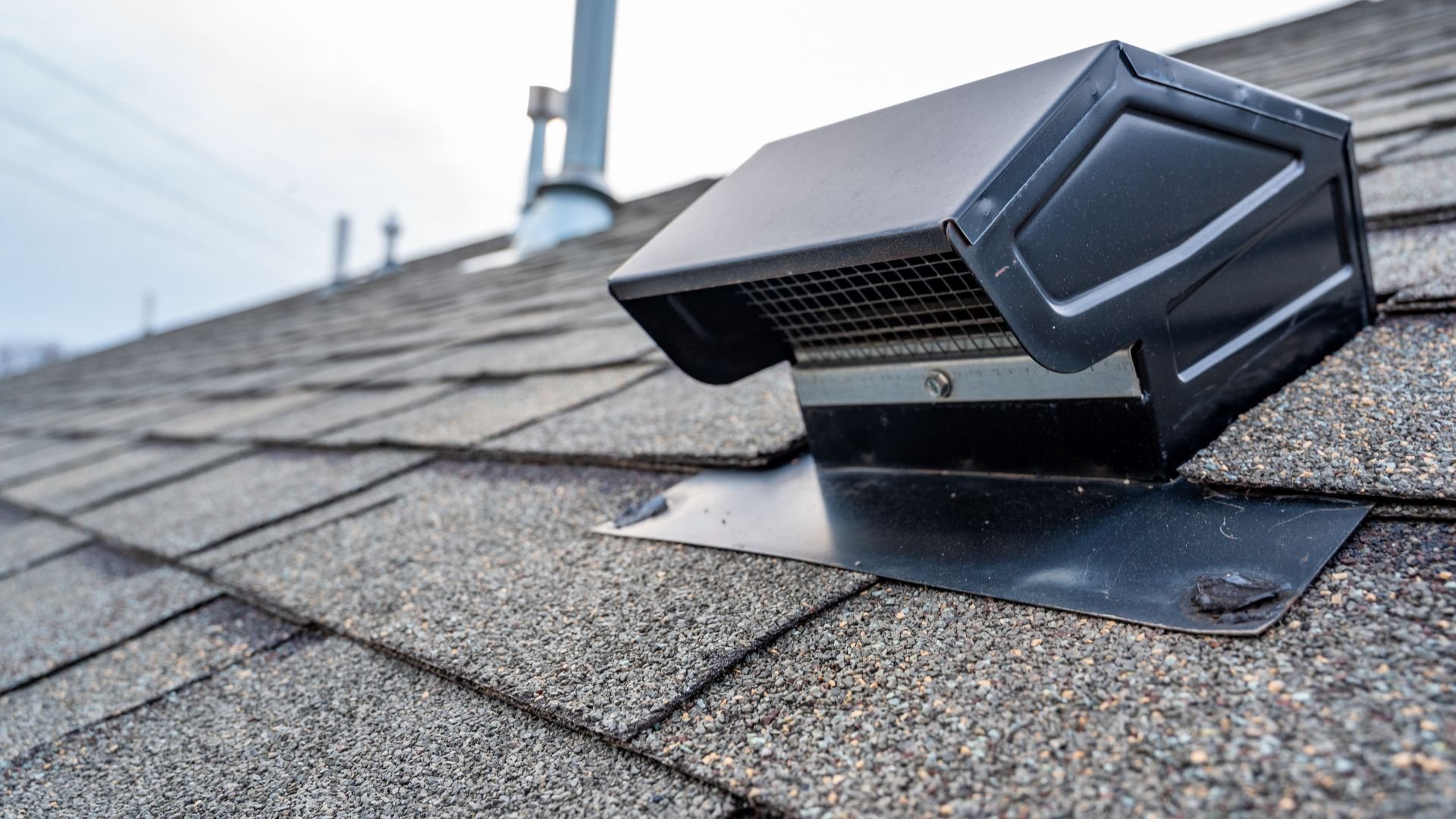 Black security camera mounted on shingle roof near metal vent