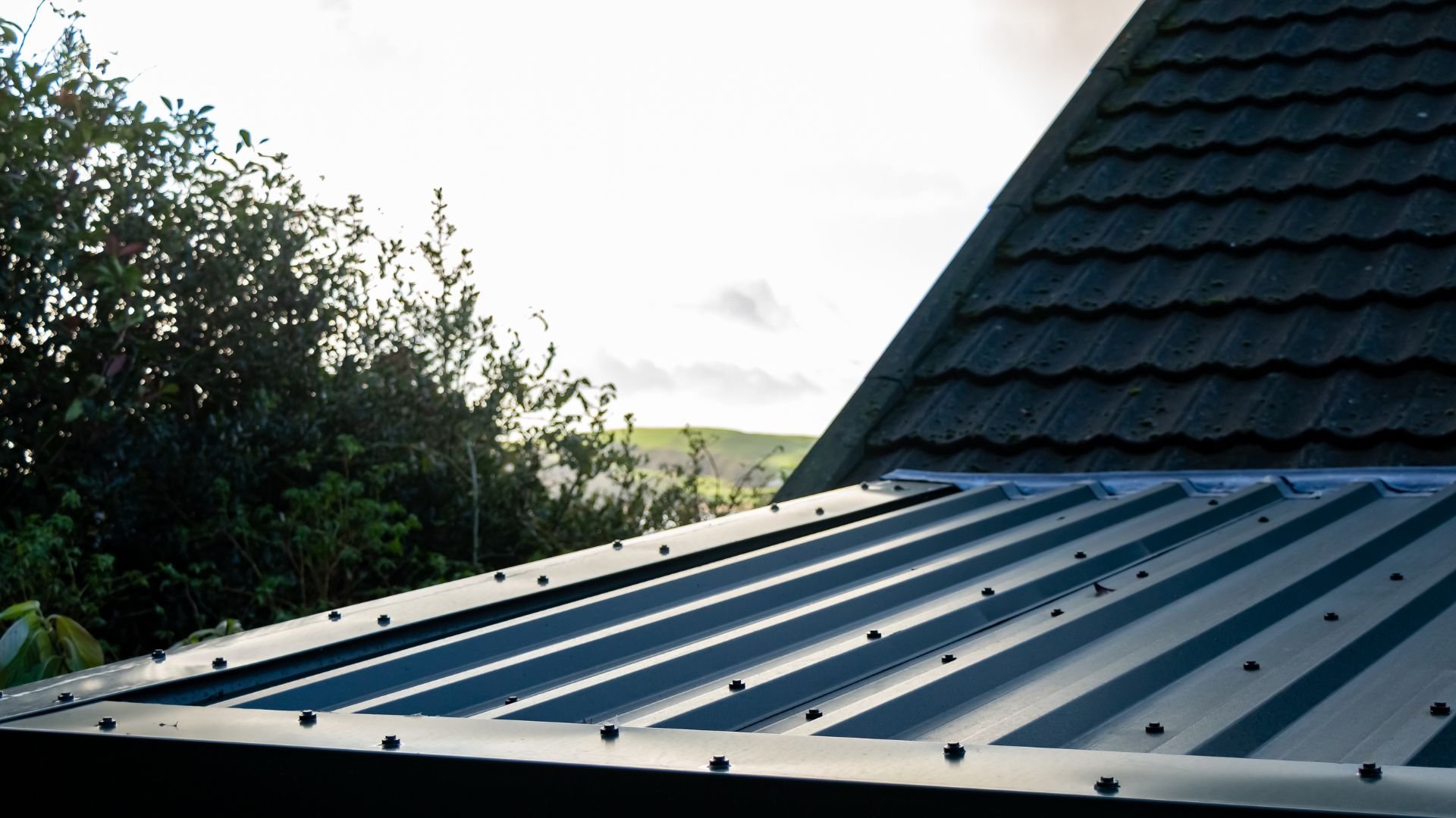 Metal roof with black tile roof and trees in background