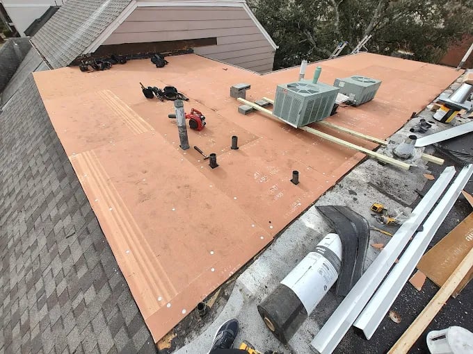 Roofing construction with tools, HVAC units, and materials on flat roof surface
