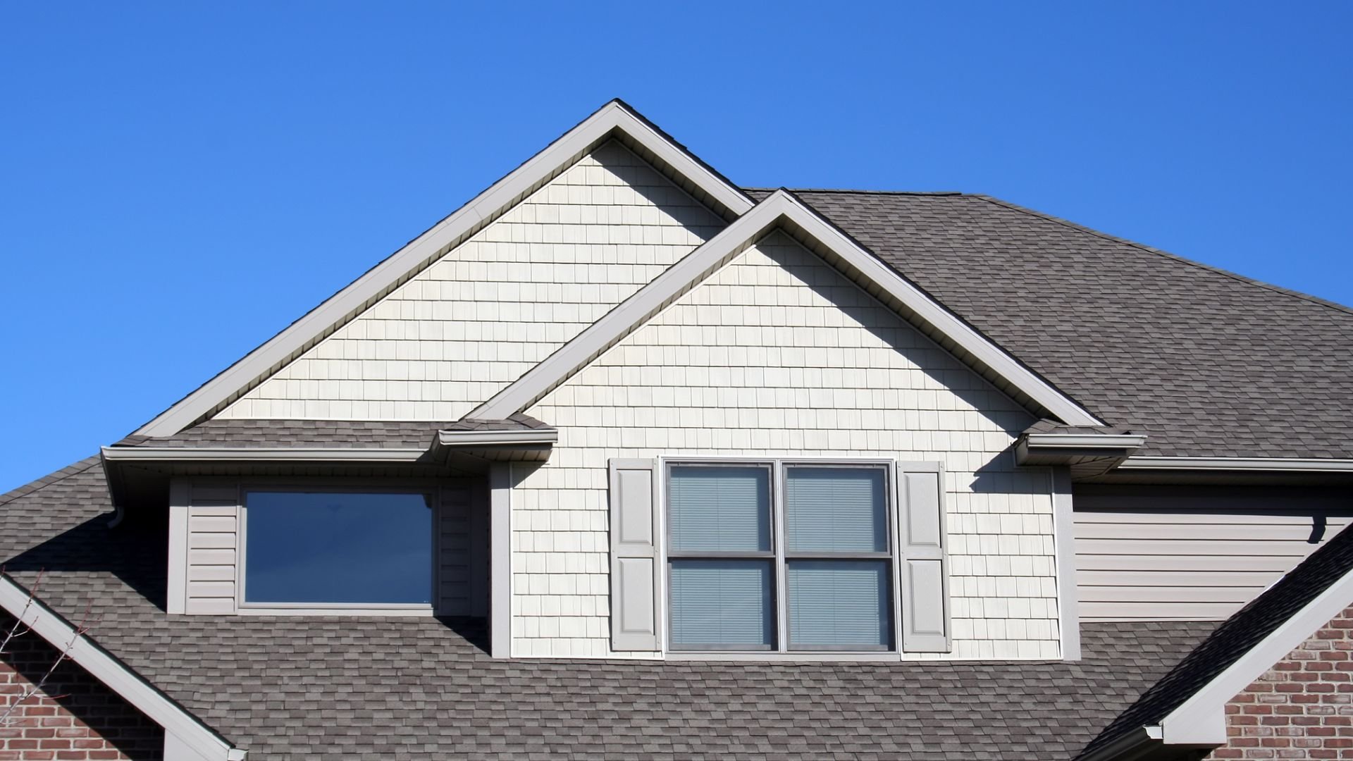 White house with gray roof, two windows with shutters, blue sky