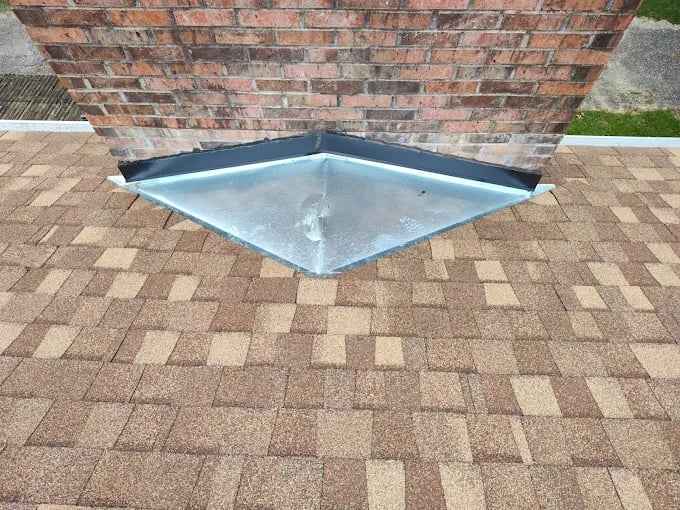 Metal roof valley flashing installed on shingle roof against brick wall