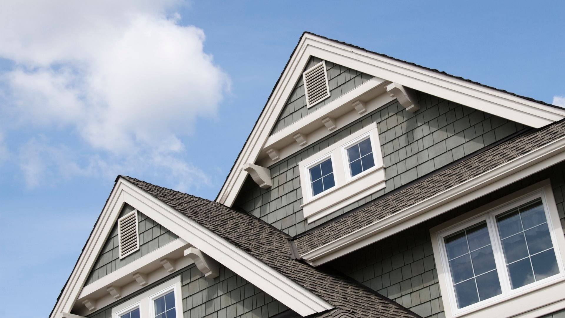 Gray shingle-style house with white trim against blue sky
